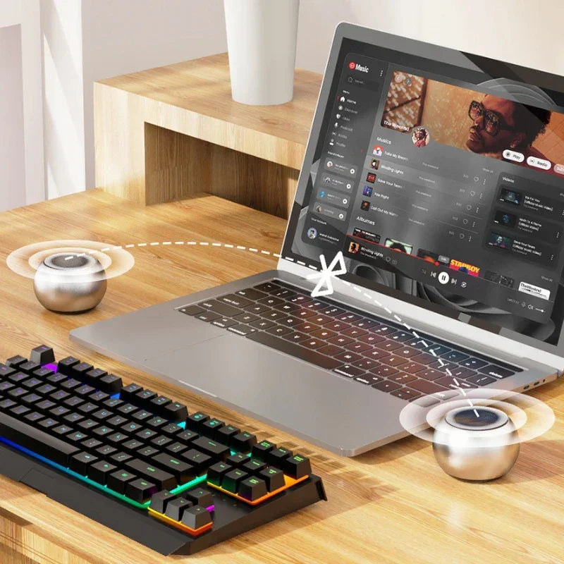 Ordinateur portable avec musique en streaming et mini enceintes sans fil connectées via Bluetooth sur bureau en bois