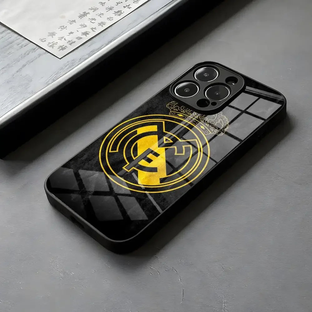Coque de téléphone noir avec logo Real Madrid en jaune, posée sur surface grise