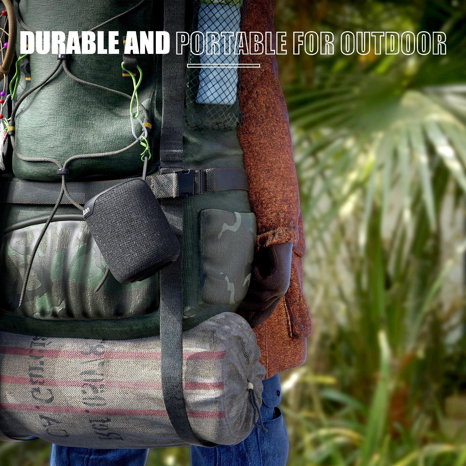 Haut-parleur portable noir accroché à un sac à dos de randonnée vert en extérieur