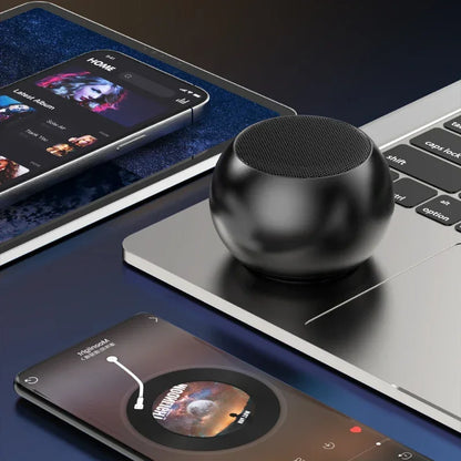 Enceinte Bluetooth noire sphérique posée sur un ordinateur portable, avec deux smartphones affichant des applications de musique