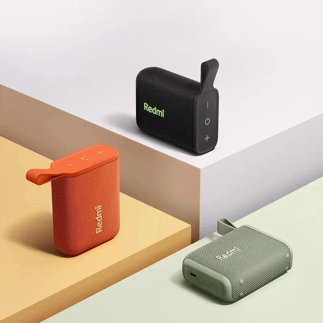 Enceintes Bluetooth Redmi compactes en noir, orange et vert sur surfaces colorées