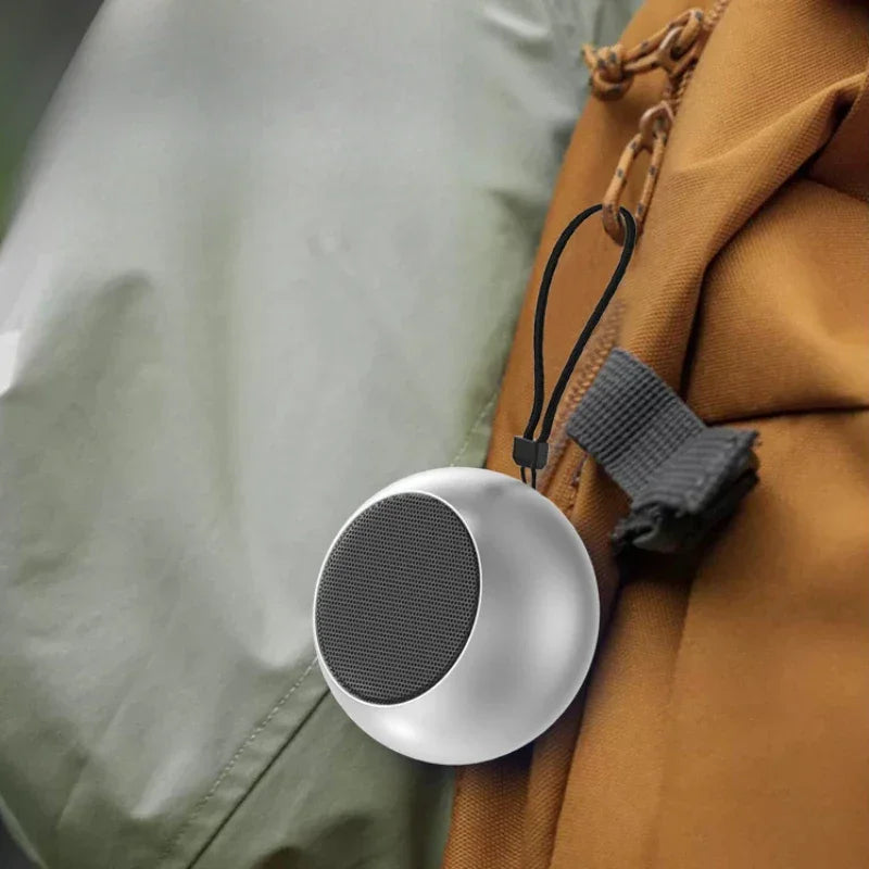 Enceinte Bluetooth portable ronde argentée suspendue à un sac à dos marron en tissu