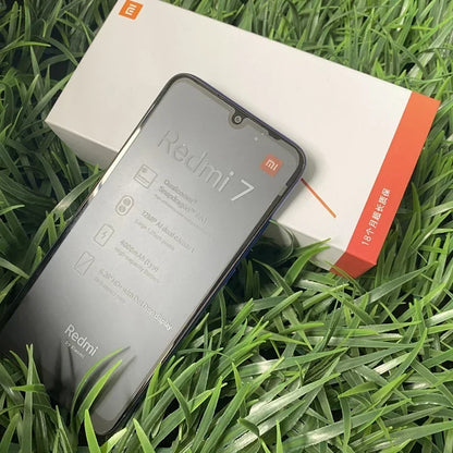 Smartphone Redmi 7 avec caractéristiques affichées, emballage blanc et orange sur fond d'herbe verte