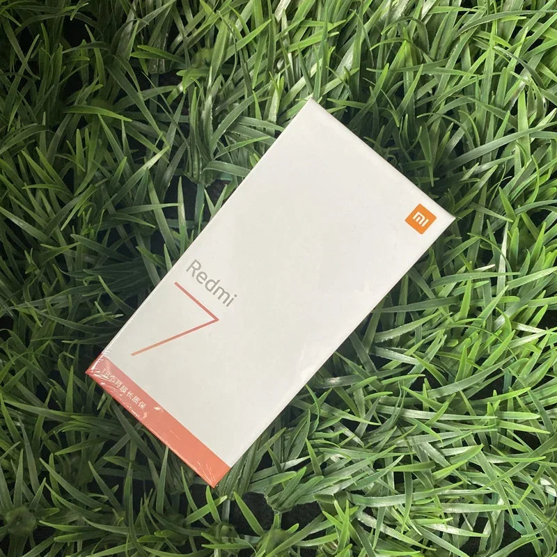 Boîte blanche Xiaomi Redmi 7 sur fond de feuilles vertes, emballage neuf