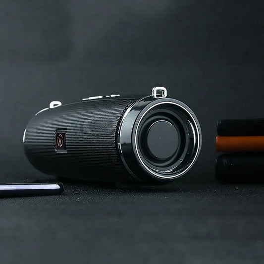 Enceinte Bluetooth portable noire posée sur surface sombre avec éléments en arrière-plan flous