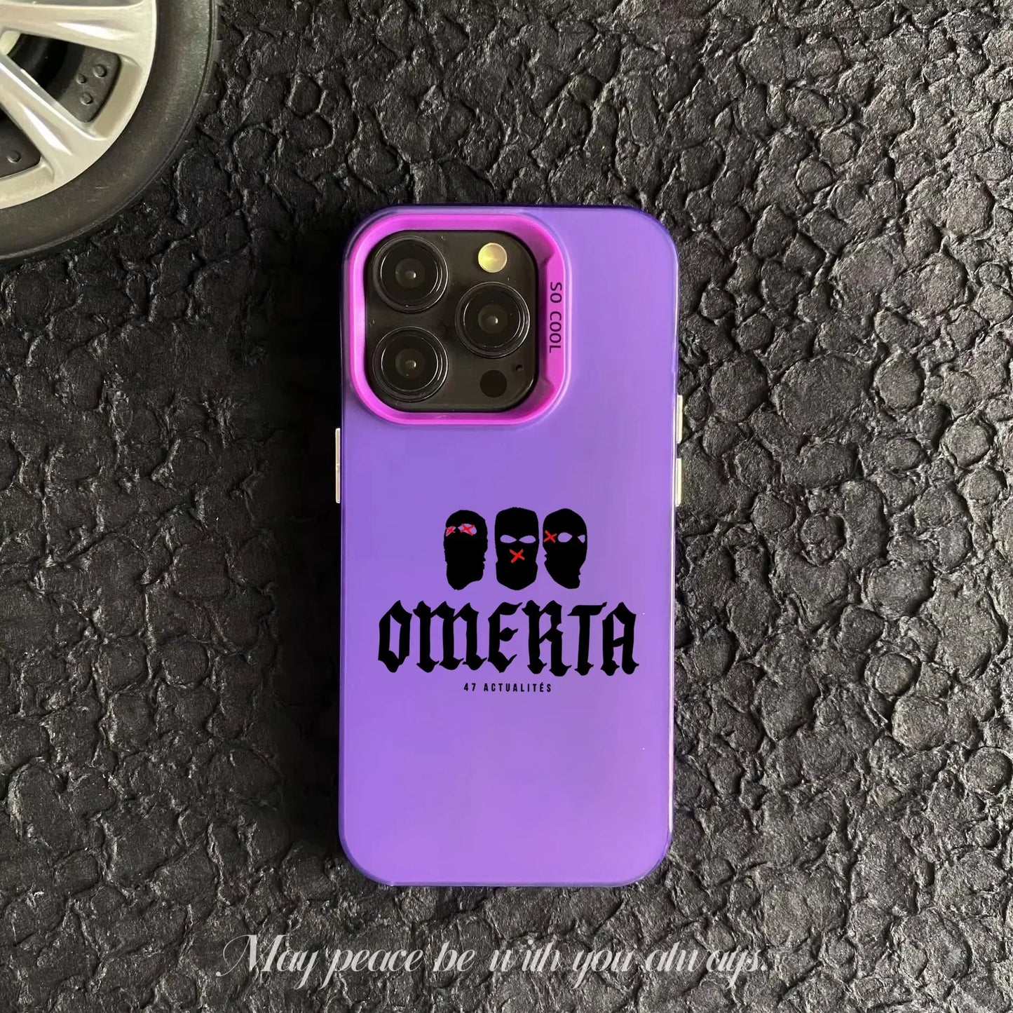Coque de téléphone violet avec design Omertà et masques noirs sur fond asphalté avec roue visible