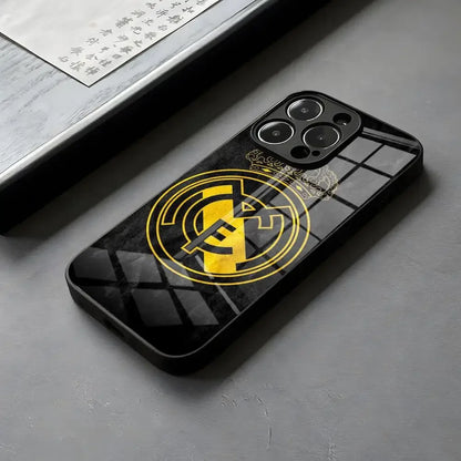 Coque de téléphone noir avec logo Real Madrid en jaune, posée sur surface grise
