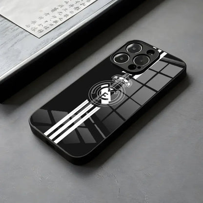 Coque de téléphone noire brillante avec logo Real Madrid et bandes blanches sur surface grise