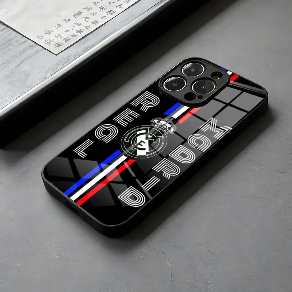 Coque de téléphone noire brillante avec motif Real Madrid et bandes bleue, blanche et rouge, posée sur surface grise