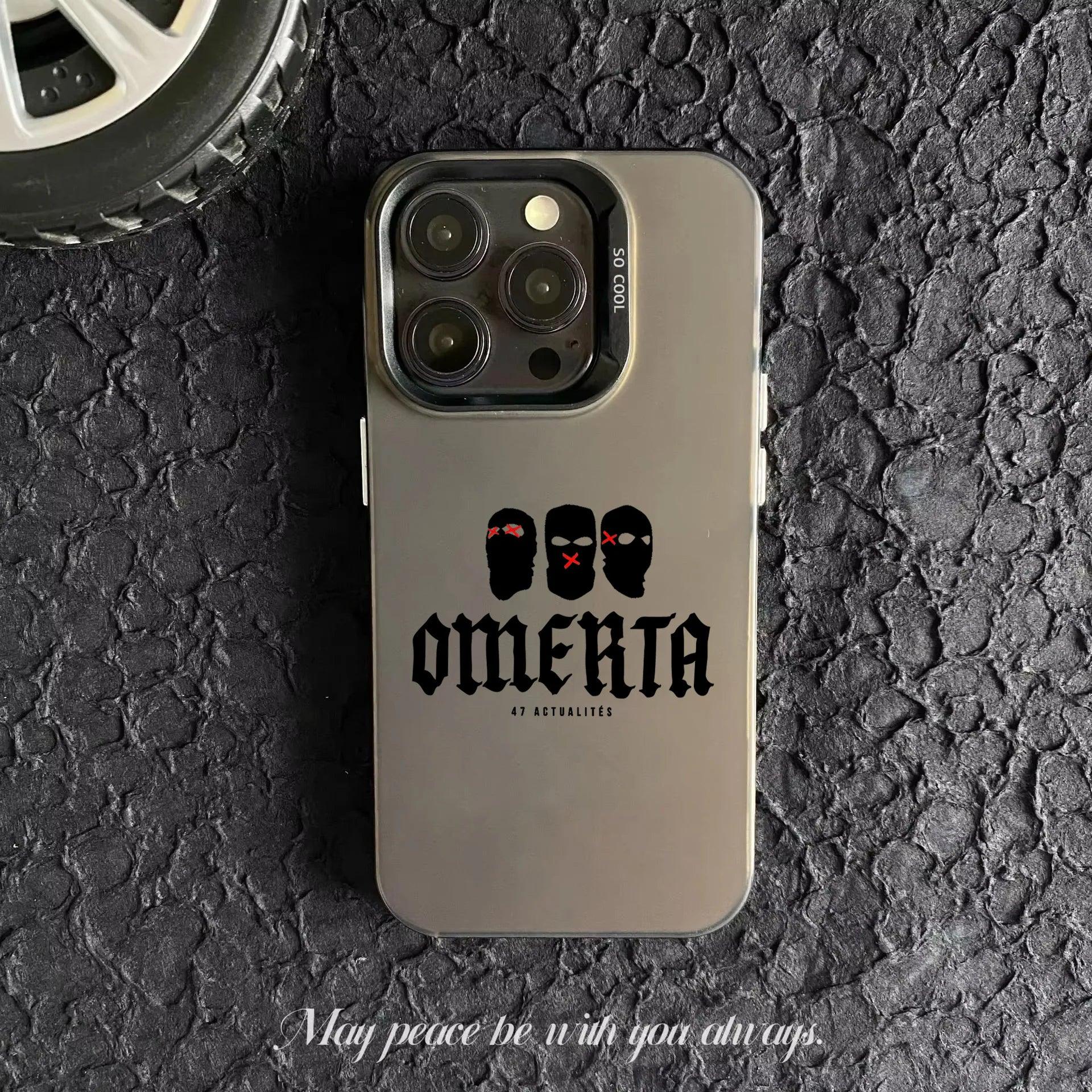 Coque de smartphone grise avec illustration de trois masques noirs et texte "OMERTA 47 ACTUALITÉS" sur sol noir texturé