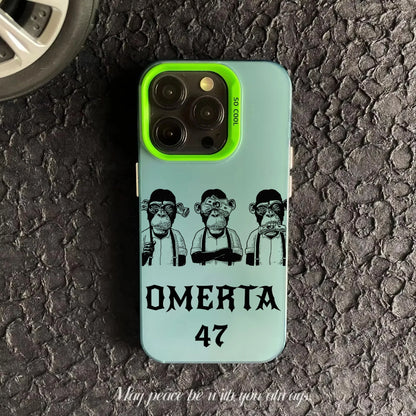 Coque de téléphone verte avec trois singes dessinés et texte OMERTA 47 sur surface asphaltée